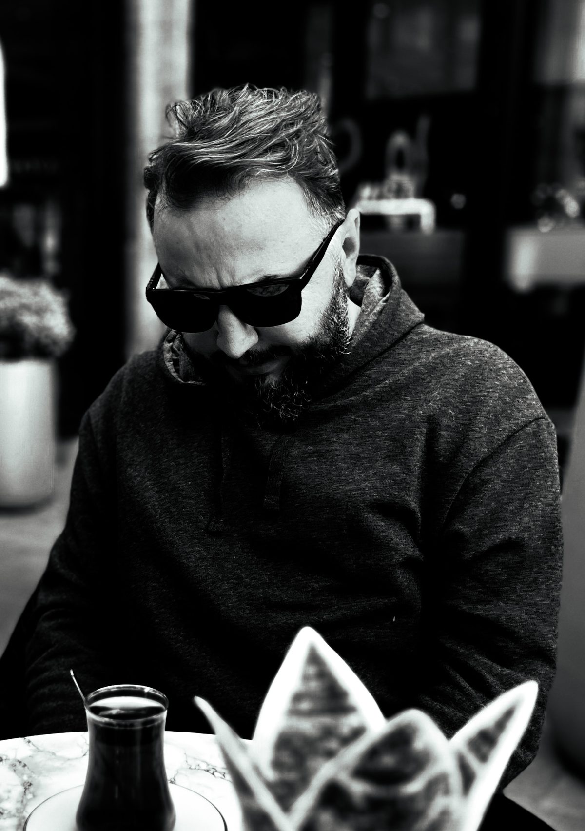 Muzaffer Demirhan Keskin in sunglasses at a café table in Istanbul, black and white portrait